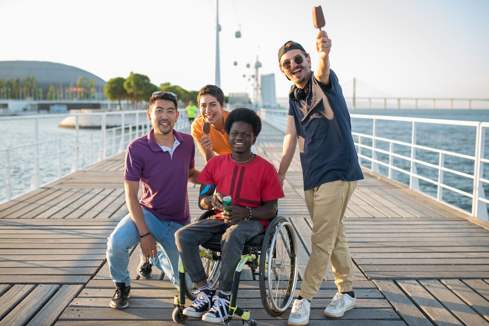 Friends laughing together on a boardwalk, one using a wheelchair
